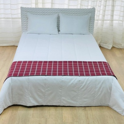 Cama com colcha branca e detalhe vermelho xadrez com duas almofadas
