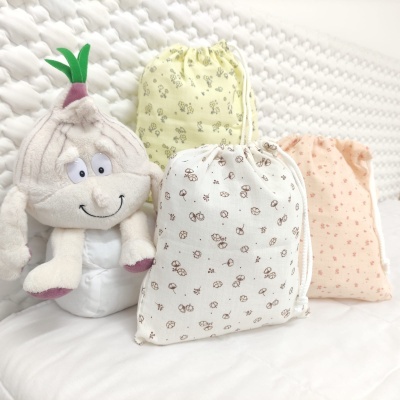 Sacos de pano estampados e peluche de alho sorridente sobre superfície branca acolchoada