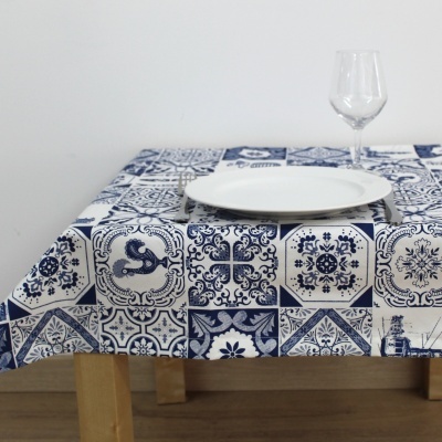 Toalha de mesa azul e branca com padrão de azulejos portugueses, prato branco e taça de vidro numa mesa de madeira clara.