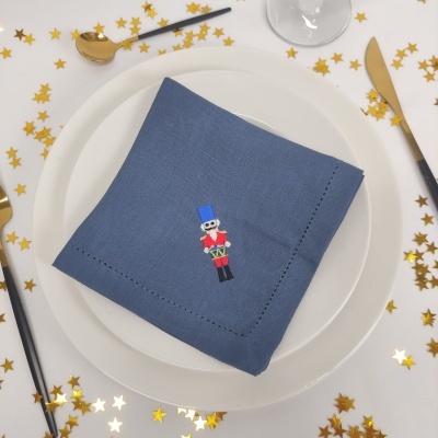 Guardanapo azul com bordado de soldado de chumbo sobre prato branco em mesa decorada com estrelas douradas