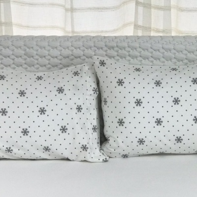 Conjunto de duas almofadas brancas com flocos de neve cinzentos sobre cabeceira acolchoada cinzenta