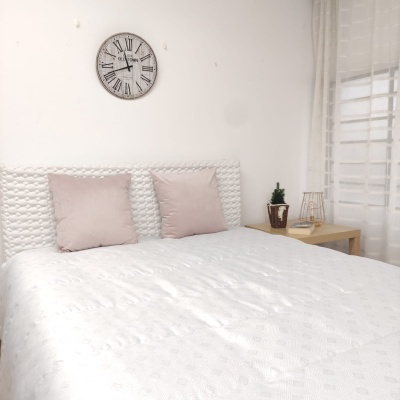 Quarto com cama de casal, almofadas cor-de-rosa, relógio de parede e mesa de cabeceira com planta