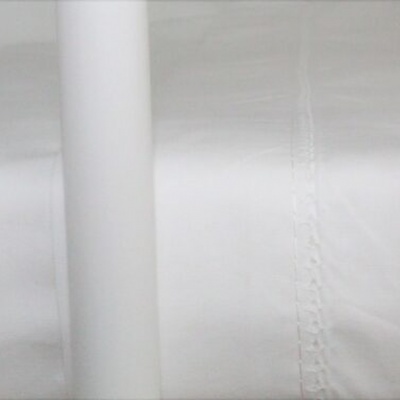 Tecido branco com costura decorativa ao lado de tubo branco