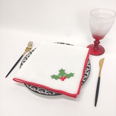 Conjunto de refeição com guardanapo branco bordado, talheres preto e dourado, prato padrão preto e branco e copo rosa texturizado.