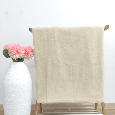 Toalha bege pendurada em estrutura de madeira com vaso branco e flores cor-de-rosa ao lado