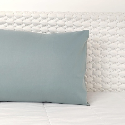 Almofada azul clara sobre cama branca com cabeceira estofada branca