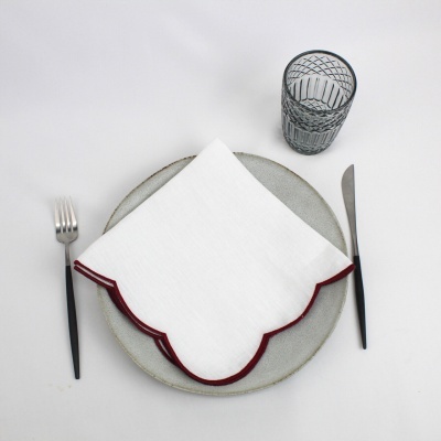 Guardanapo branco com borda vermelha sobre prato cinza, garfo, faca e copo transparente
