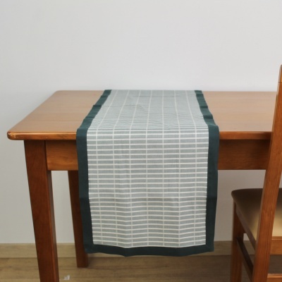 Caminho de mesa tecido branco com padrão e borda verde escuro numa mesa de madeira