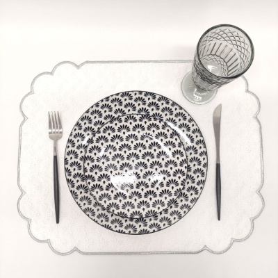 Conjunto de jantar com prato decorado, talheres e copo de vidro sobre sousplat branco.