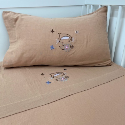 Fronha e lençol bege com bordados de personagem infantil e flores pequenas em cama branca