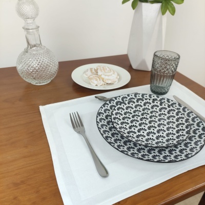 Mesa posta com prato e tigela com padrão preto e branco, talheres, copo cinzento, garrafa de vidro e prato com merengues