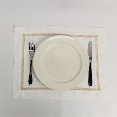 Prato branco com garfo e faca sobre individual branco com borda bege