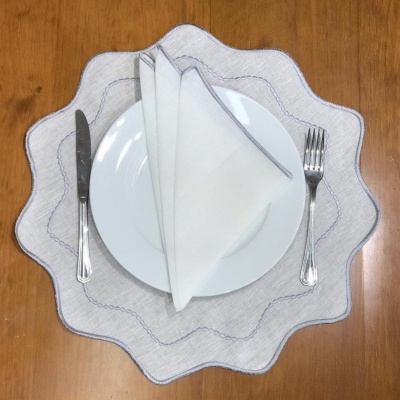 Conjunto de jantar com prato branco, sousplat cinza ondulado, guardanapo branco e talheres sobre mesa de madeira