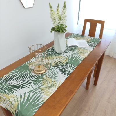 Mesa de madeira com toalha de mesa com padrão de folhas, vaso branco com flores e castiçal dourado