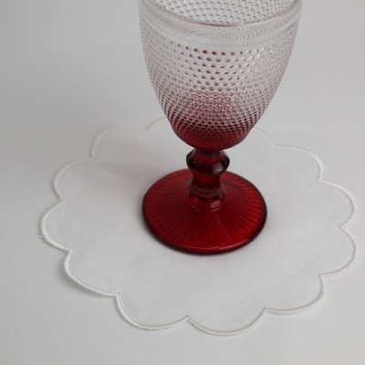 Copo de vidro vermelho com padrão texturizado sobre sousplat branco em formato de flor