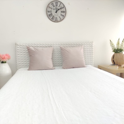 Cama com almofadas cor de rosa, colcha branca e relógio de parede com números romanos