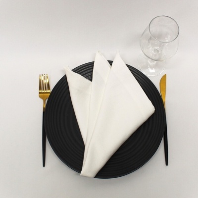 Mesa posta com prato preto, guardanapo branco, talheres pretos com dourado e copo de vidro