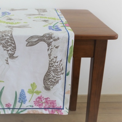 Toalha de mesa branca com coelhos e flores sobre mesa de madeira.
