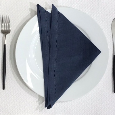 Conjunto de talheres, prato branco e guardanapo azul escuro sobre superfície branca