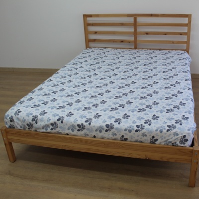 Cama de madeira com colchão com capa de flores sobre chão de madeira e parede branca