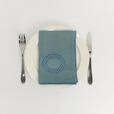 Guardanapo azul claro com padrão geométrico em prato branco com talheres.