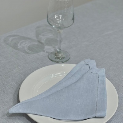 Prato branco com guardanapo cinzento e copo de vidro transparente em mesa cinzenta.