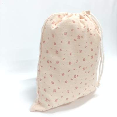 Saco de pano bege com pequenas flores cor-de-rosa e cordão branco para fechar.