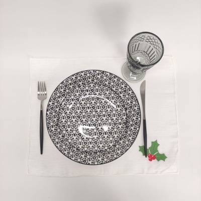 Conjunto de jantar com prato preto e branco, talheres pretos, copo transparente e individual branco com decoração de folhas e bagas vermelhas