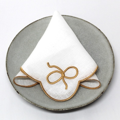 Guardanapo branco com bordado dourado em prato cinza