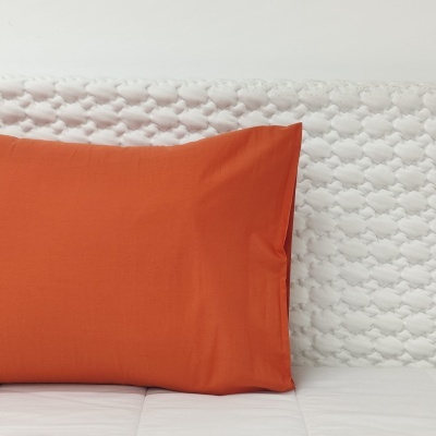 Travesseiro com fronha laranja sobre cama com cabeceira branca texturizada