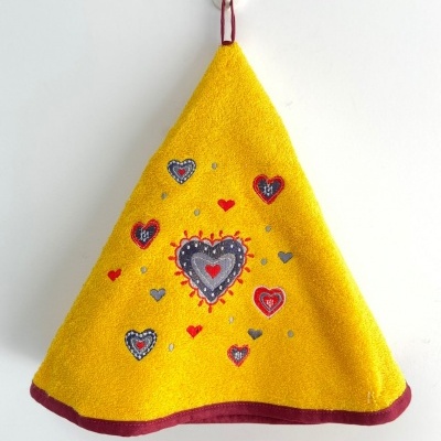 Pano de cozinha amarelo triangular com corações bordados pendurado na parede