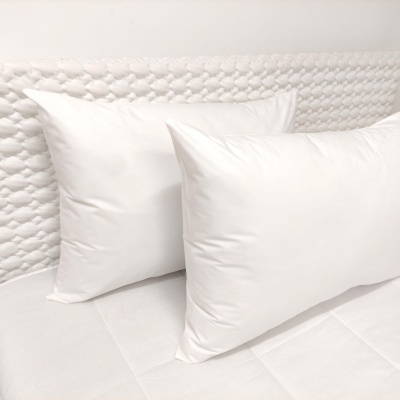 Dois almofadas brancas retangulares e quadradas sobre colchão e cabeceira branca
