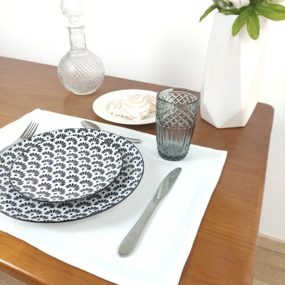 Conjunto de pratos, copo e talheres numa mesa com jarro branco e planta