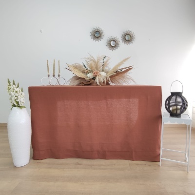 Mesa vestida com toalha terracota e decoração floral seca, castiçais dourados, vaso branco com flores, lanterna preta e espelhos redondos na parede