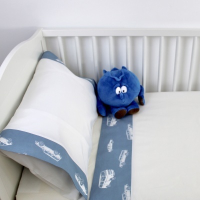 Berço branco com almofada branca e azul decorada com carros e peluche azul com olhos grandes