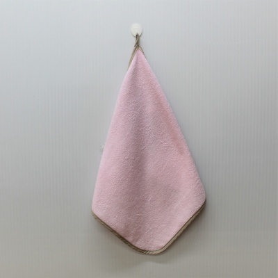 Toalha cor-de-rosa com borda castanha pendurada num suporte branco num fundo claro