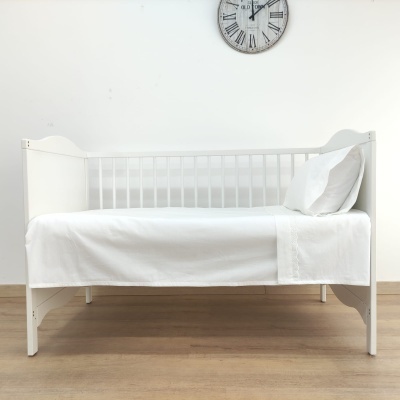 Cama de criança branca com roupa de cama branca e relógio de parede com números romanos