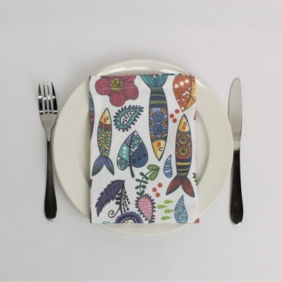 Guardanapo com padrão de peixes e flores sobre prato branco com talheres