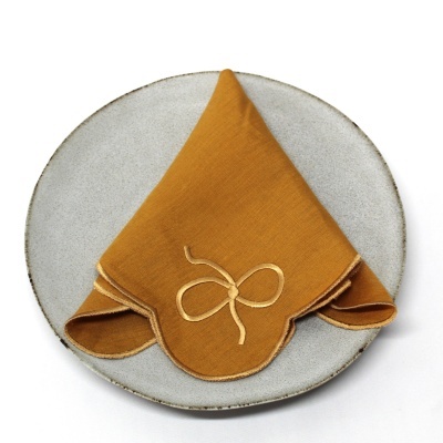 Guardanapo mostarda bordado sobre prato cinza de cerâmica