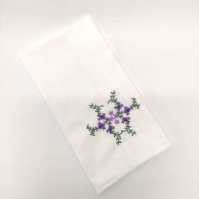 Toalha branca com bordado de flores roxas e folhas verdes