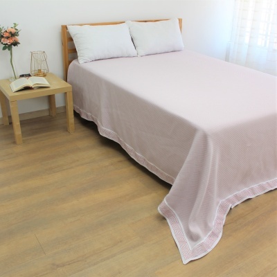 Cama de madeira com colcha rosa clara e almofadas brancas ao lado de mesa de cabeceira com flores e livro