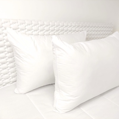 Dois almofadões brancos sobre colchão branco com cabeceira texturizada branca
