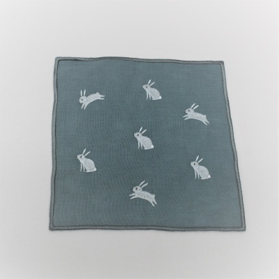 Pano cinzento quadrado com bordados de coelhos brancos.