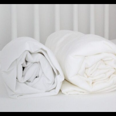 Dois edredões brancos enrolados lado a lado com cabeceira branca ao fundo