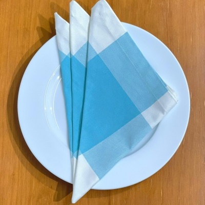 Três guardanapos de tecido azul e branco sobre prato branco em mesa de madeira.