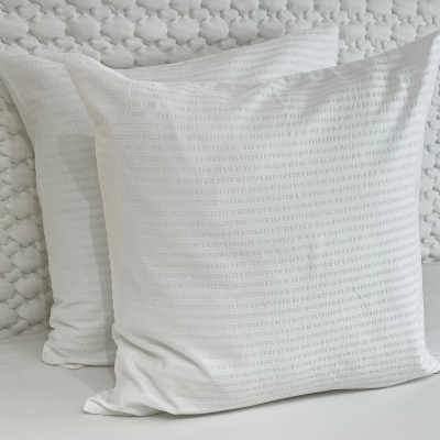 Duas almofadas brancas com padrão texturizado colocadas sobre fundo acolchoado branco