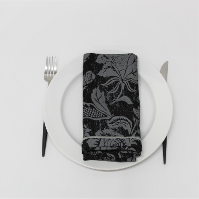 Toalhete preto com padrão floral sobre prato branco com talheres ao lado