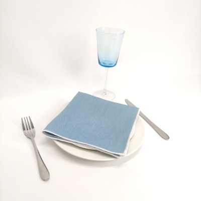 Conjunto de jantar com prato branco, guardanapo azul, talheres de metal e copo azul