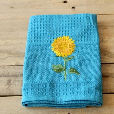 Toalha azul clara com bordado de girassol sobre superfície de madeira clara