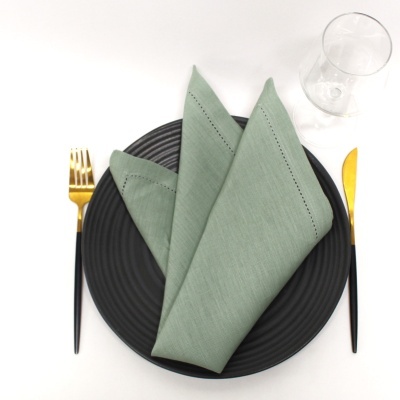 Conjunto de prato preto com guardanapo verde, talheres preto e dourado e copo transparente